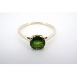 A contemporary 9ct gold and precious green gemstone dress ring, having a central round-cut
