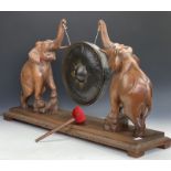 A late 19th Century carved wood and brass dinner gong, modelled as a pair of confronting
