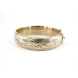 A 9 ct gold hinged bangle, of shallow D-section and foliate scroll engraved, 1962, 26.6 g, 59 mm x