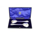A cased pair of George V silver Trefid pattern serving spoons, with scrolling decoration to the back