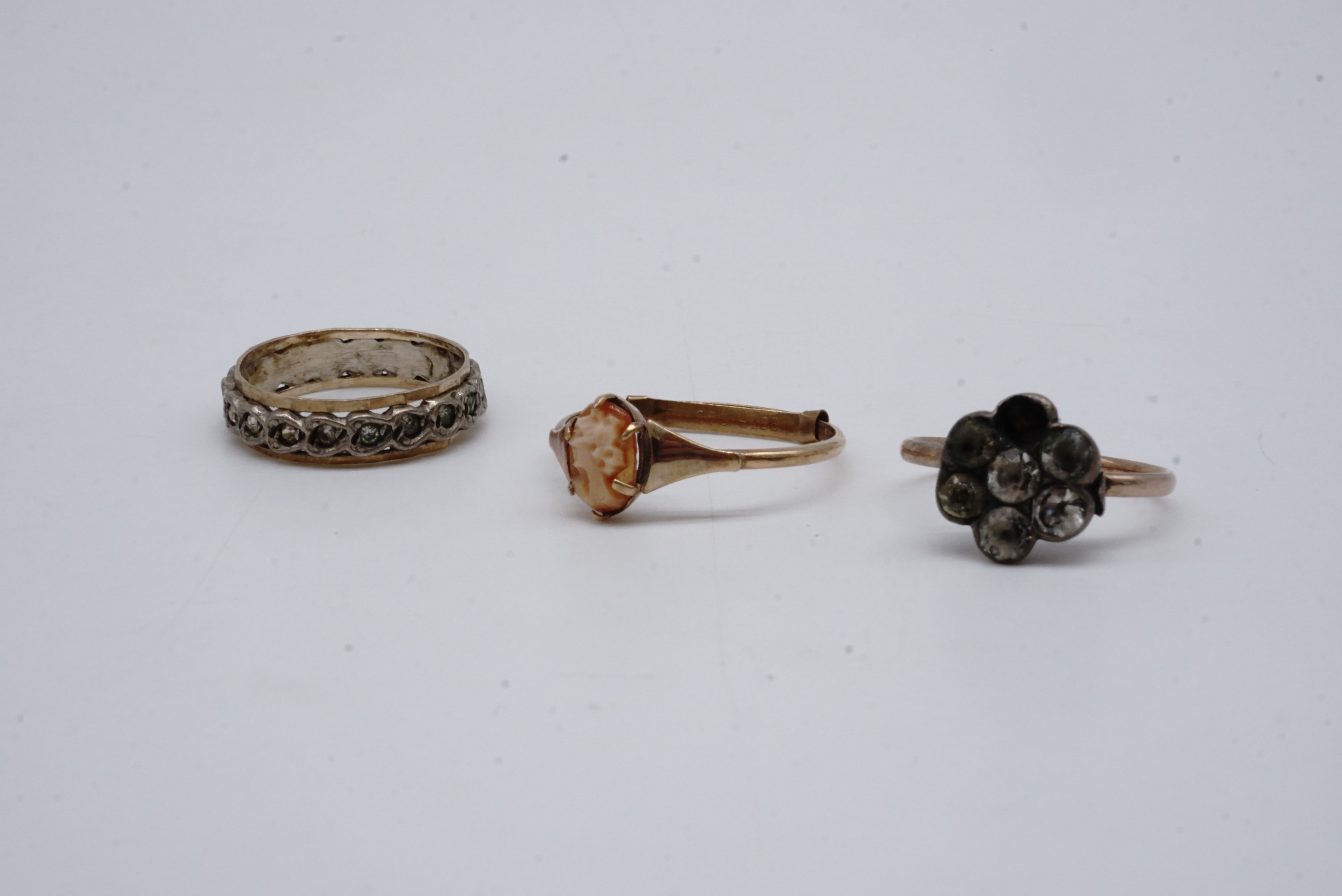 Three vintage yellow metal rings, one with a carved shell cameo claw set to the face, one eternity