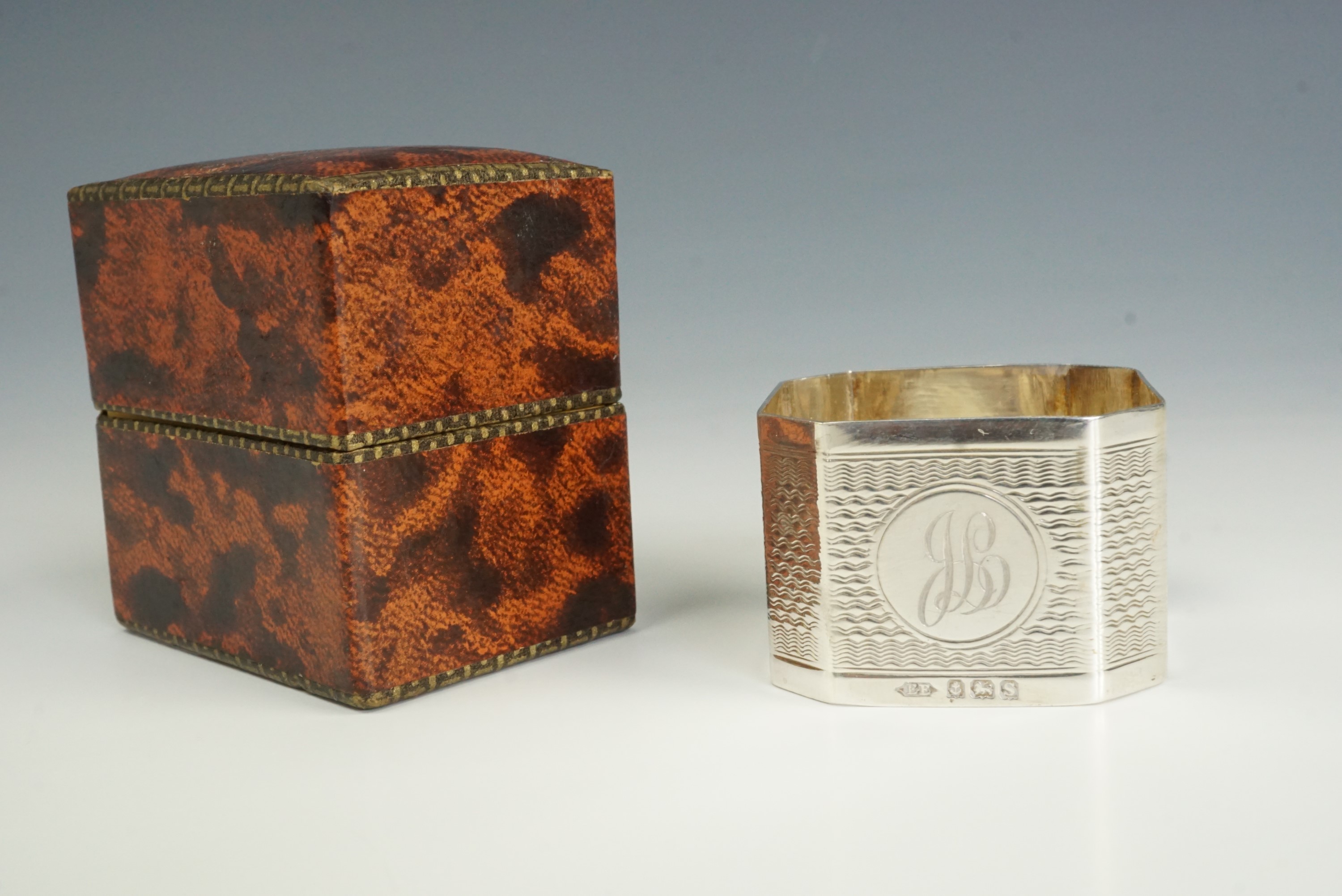 An early 20th Century silver napkin ring, of square section with canted corners, bearing engine-