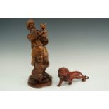 A carved wooden figure of a hunter playing with a young animal together with a carved wooden lion,