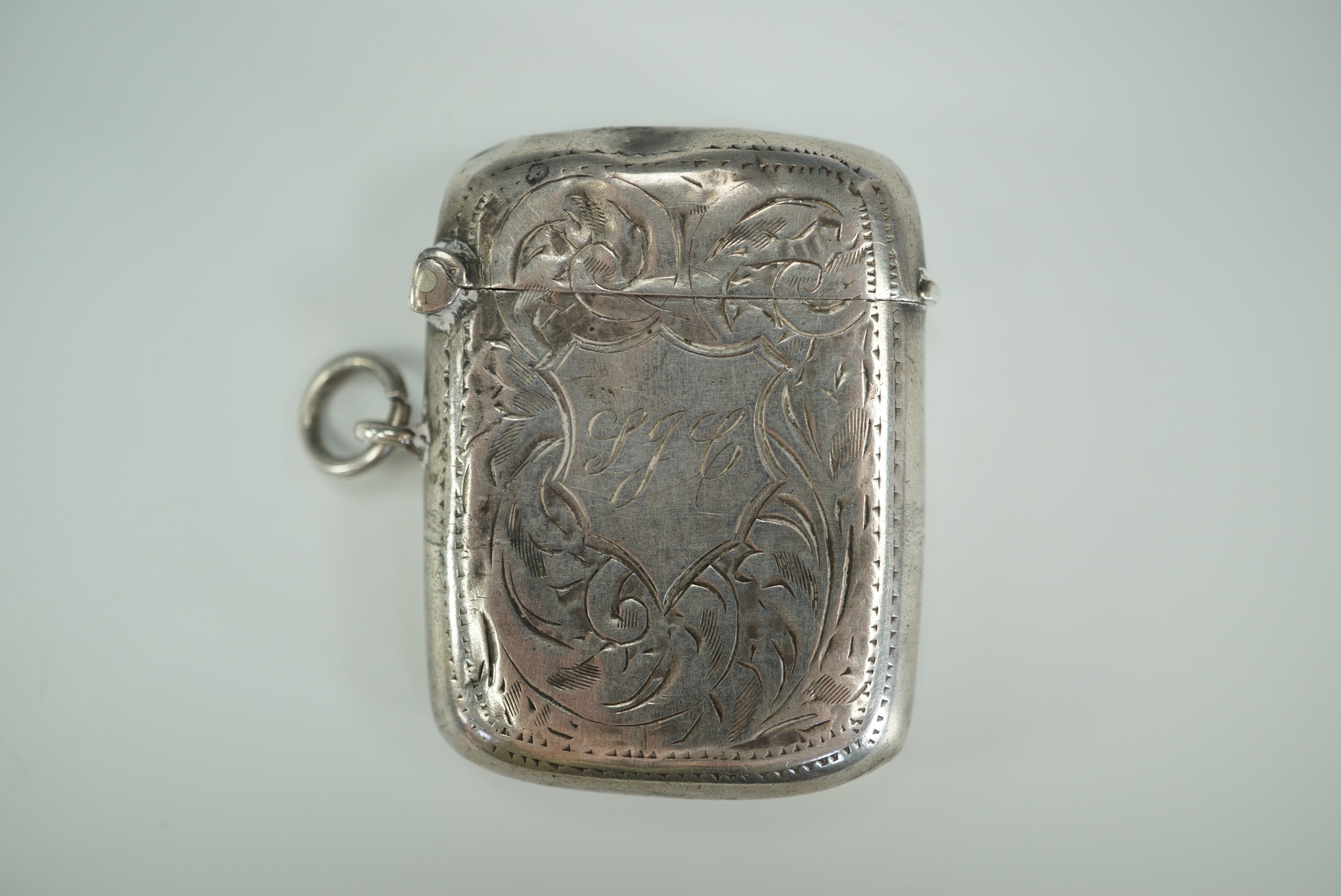 A George V silver Vesta case, contoured cushion shaped and foliate scroll engraved