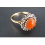 A coral, diamond and 18 ct gold cluster ring, the coral cabochon of approx 7 mm crown set within a