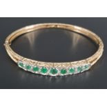 An emerald, diamond and 9 ct gold hinged bangle, comprising nine graded facet-cut emeralds, the