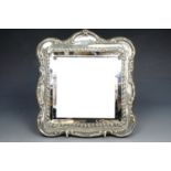 An Edwardian silver dressing table mirror, having a bevel-edged square mirror plate and moulded