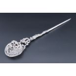 An early 20th century cast silver mote spoon, having rococo influenced bowl, held in the mouth of