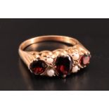 A vintage garnet and pearl ring, comprising a central oval garnet of approximately 7 mm x 5 mm,