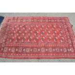 Pakistan rug of Bokhara design with three rows of gols on a wine red ground, 6ft 4ins x 4ft