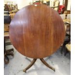 Circular mahogany tilt top pedestal dining table with a turned column support and quadruped base