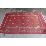 Afghan rug with a repeating hooked medallion design on a wine red ground with borders (some wear),