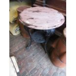 Black painted cast iron pub table, the circular wooden top above three mask head supports, 23ins