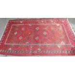 Afghan rug with a repeating hooked medallion design on a wine red ground with borders (some wear),