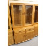 Modern Ercol light elm side cabinet with two bevelled glass doors enclosing shelves above two