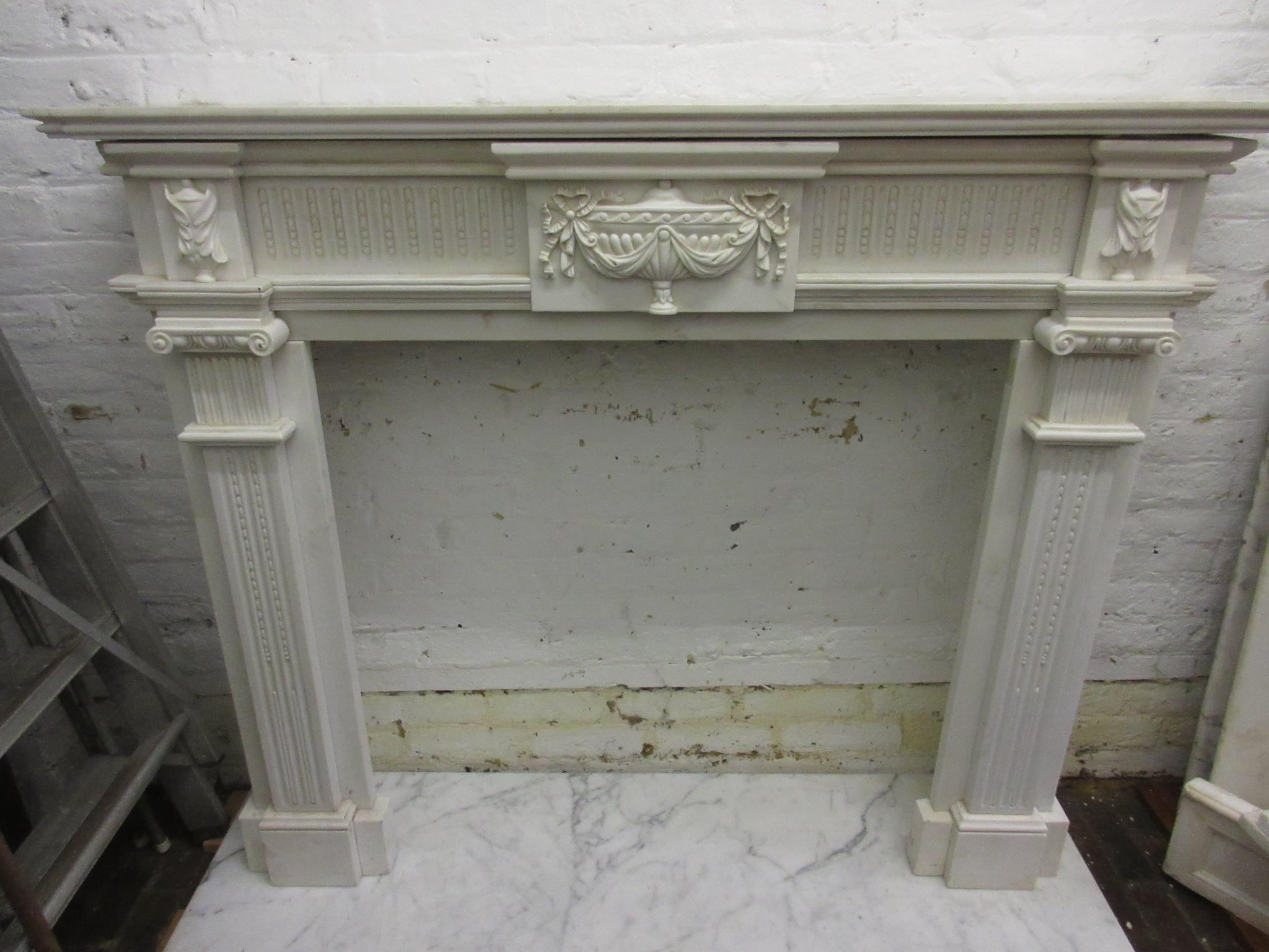Large white marble fire surround having a moulded mantelpiece, above a central urn with bows and