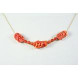 A CARVED CORAL NECKLET formed with three carved coral flowerheads and six coral cabochons, in