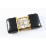 A GILT METAL TRAVELLING CLOCK BY MOVADO the signed square-shaped dial with baton numerals, in a