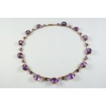 AN AMETHYST AND GOLD NECKLACE formed with graduated oval-shaped amethysts and smaller circular-