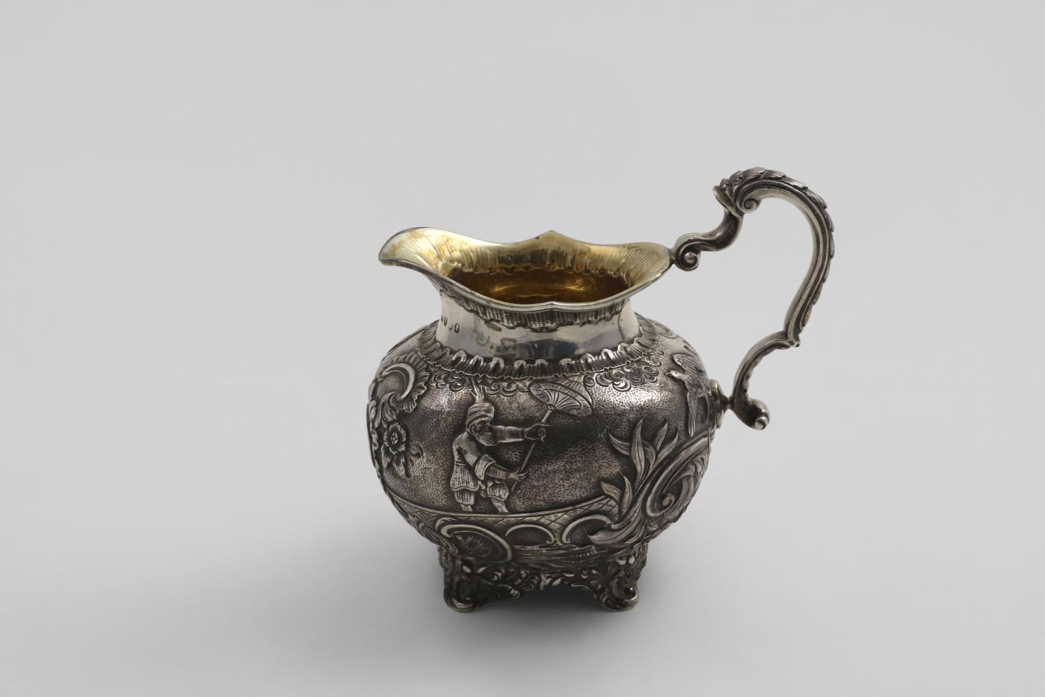 A GEORGE III MILK JUG with decorative feet, a shell-decorated handle and an oviform body with