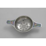 AN EARLY 20TH CENTURY TEA STRAINER with two lug handles, each decorated with enamelled flowers in