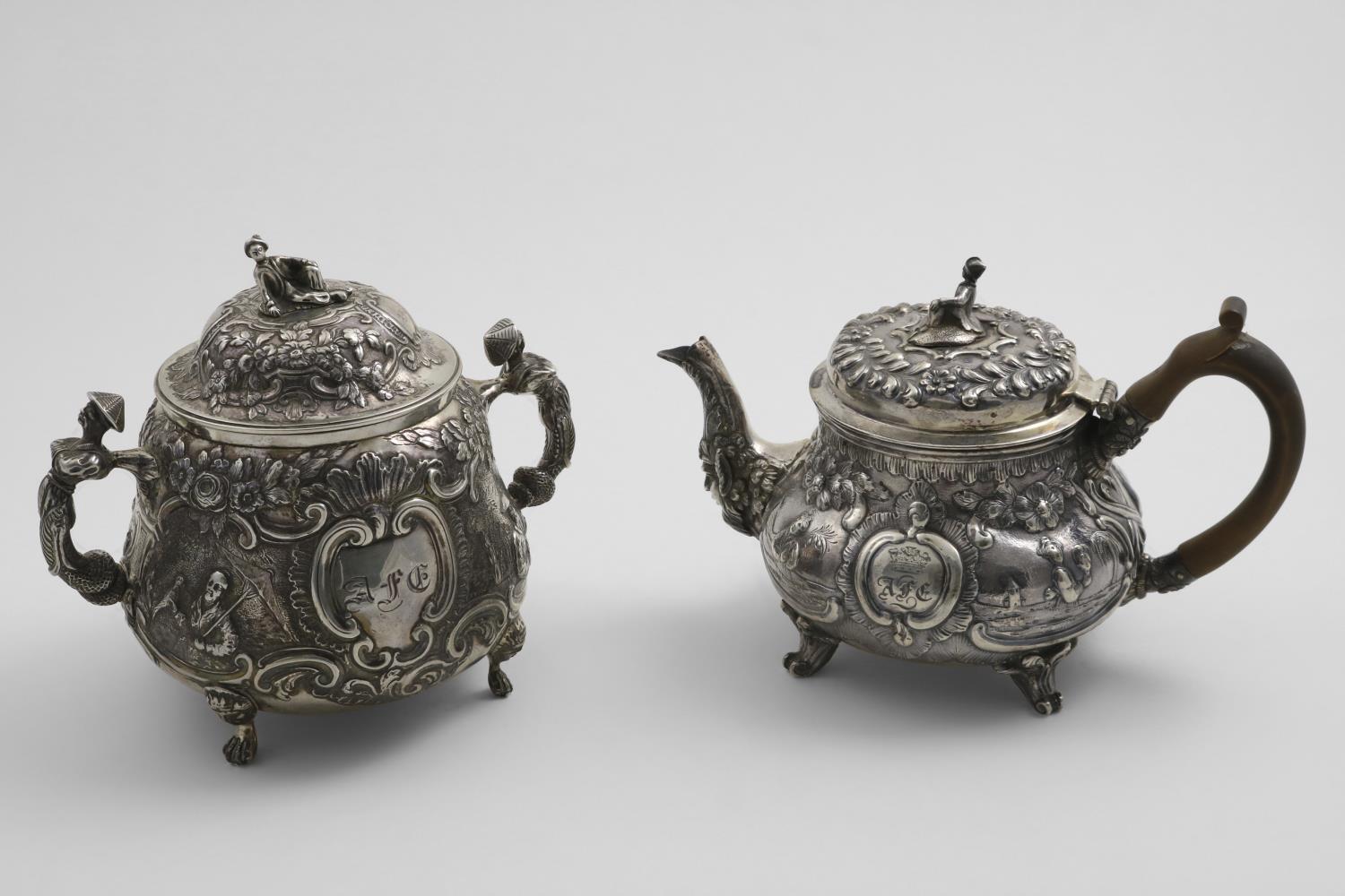 A GEORGE III SMALL REPOUSSE-WORK TEA POT with chinoiserie decoration and four feet, the cartouches