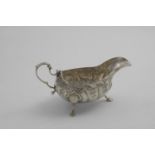 A GEORGE III IRISH SAUCE BOAT on three legs with chased trailing flowers and fluting, maker's