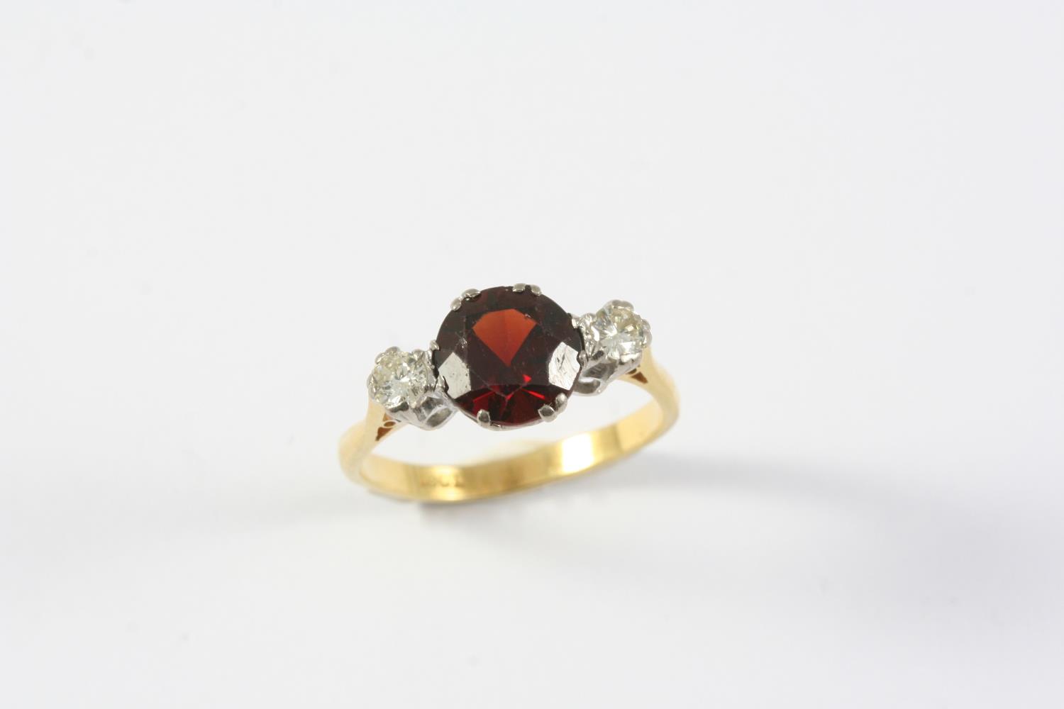 A GARNET AND DIAMOND THREE STONE RING the circular-cut garnet is set with two circular-cut diamonds,