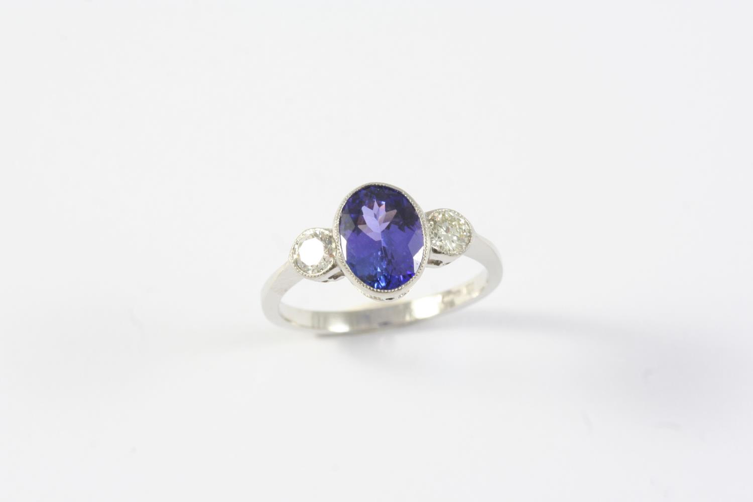 A TANZANITE AND DIAMOND THREE STONE RING the oval-shaped tanzanite is set with two circular-cut