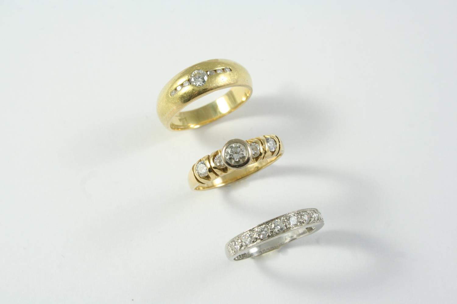 A DIAMOND SOLITAIRE RING the circular-cut diamond is collet set, with two circular-cut diamonds to