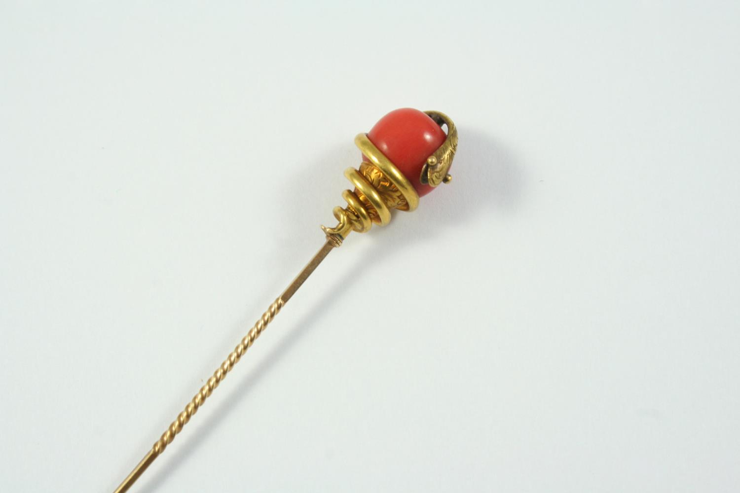 A CORAL AND GOLD SNAKE STICK PIN mounted with a coral bead entwined by a gold snake, 8.5cm long