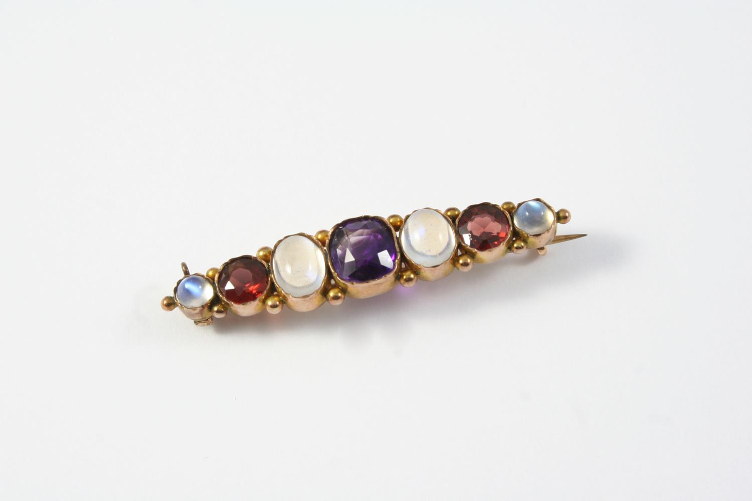 A MOONSTONE, AMETHYST AND GARNET BROOCH mounted with a cushion-shaped amethyst, two circular garnets