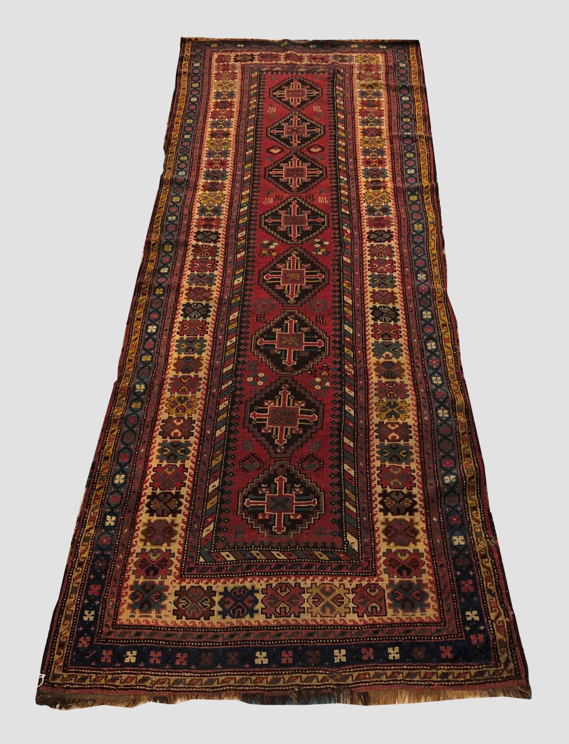 A KARABAGH LONG RUG, the raspberry field with columns of stepped medallions surrounded by