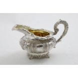 A GEORGE IV / WILLIAM IV EMBOSSED CREAM JUG with a squat circular body and decorative feet, with