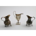 A GEORGE II BALUSTER CREAM JUG on three legs with repousse-work, floral scroll decoration & a vacant