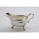 A GEORGE II SAUCE BOAT on three scroll feet, with a plain moulded rim and a leaf-capped, scroll