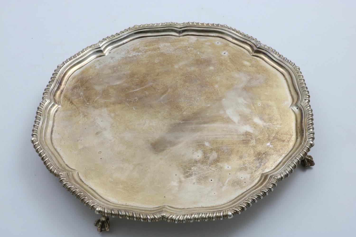 A GEORGE V SALVER of shaped circular outline with a gadrooned border and ball & claw feet, by