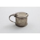 A GEORGE IV MUSTARD POT with a leafy scroll handle, a gadrooned rim & incised concentric rings on