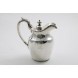 A GEORGE IV IRISH HOT WATER JUG with a helmet-shaped rim, reeded C-scroll handle, and a hinged cover