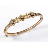 A VICTORIAN GOLD AND PEARL SET HALF HINGED BANGLE set to one side with three flowerhead clusters