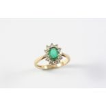 AN EMERALD AND DIAMOND CLUSTER RING the oval-shaped emerald is set within a surround circular-cut