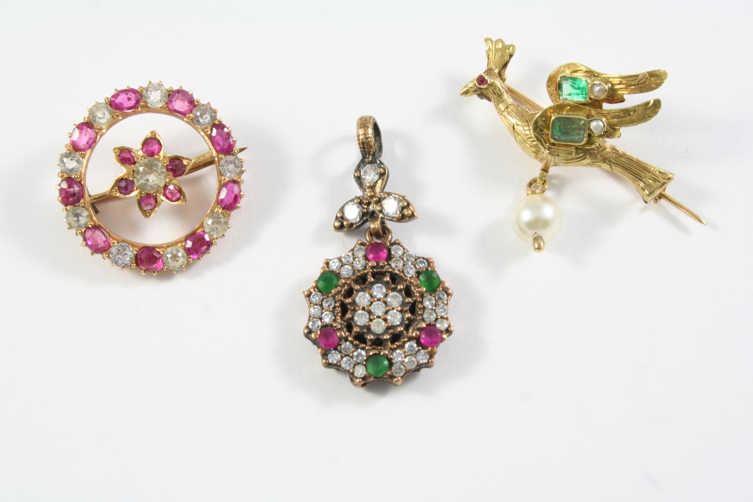 A GOLD AND GEM SET BIRD BROOCH mounted with two emeralds and suspending an untested pearl drop,