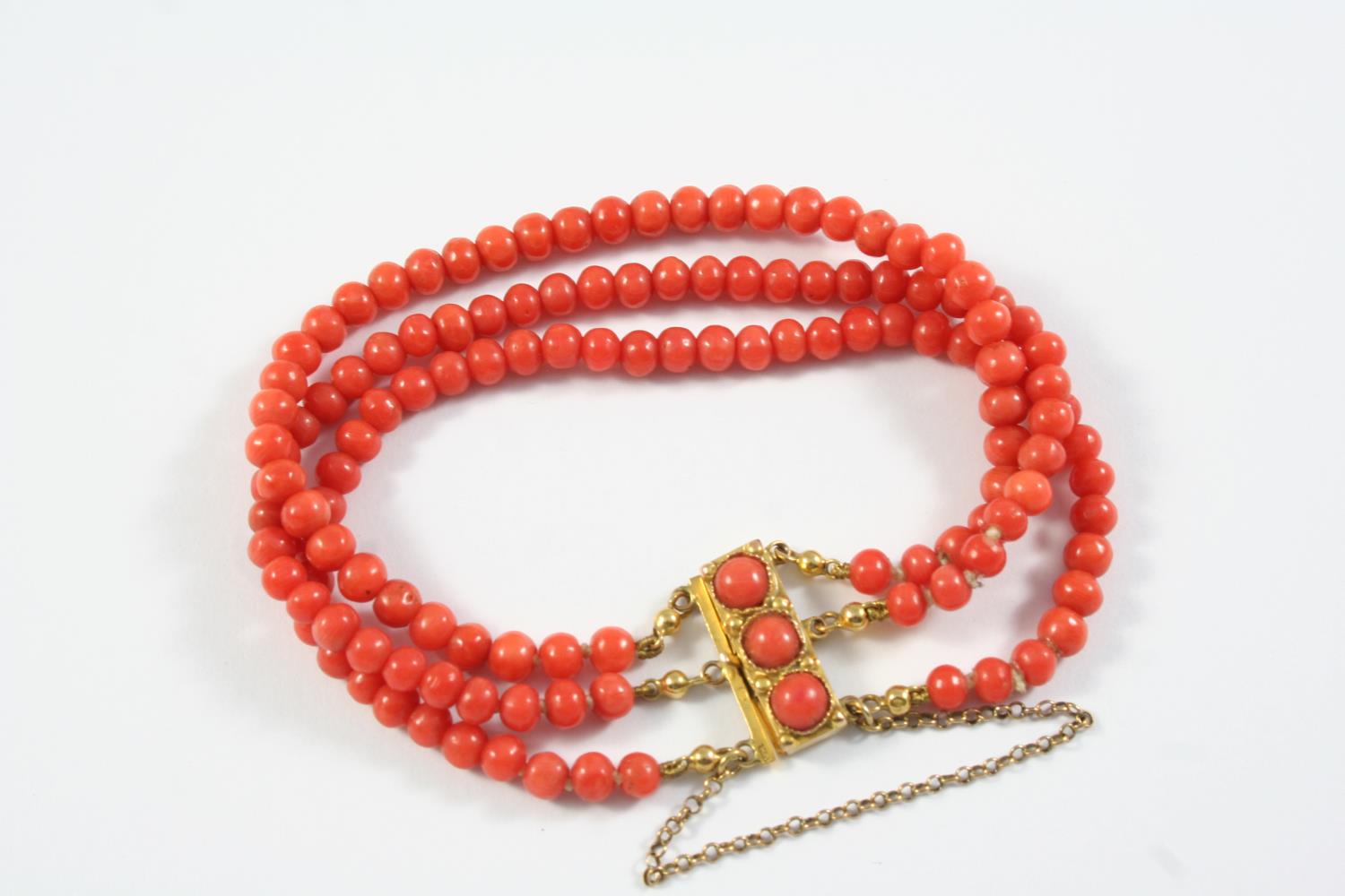 A THREE ROW UNIFORM CORAL BEAD BRACELET the coral beads are set to a gold rectangular-shaped