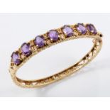 AN AMETHYST AND GOLD HALF HINGED BANGLE the openwork scrolling mount is set with seven oval-shaped