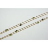 A 9CT GOLD LONG GUARD CHAIN mounted alternately with oval-shaped and pear-shaped green