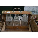 VICTORIAN OAK THREE BOTTLE TANTALUS, THE CUT GLASS DECANTERS AND STOPPERS WITH WHITE METAL SPIRIT