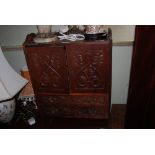 ARTS AND CRAFTS STYLE TABLE CABINET WITH FOLIATE CARVED CUPBOARD DOORS ABOVE TWO LONG DRAWERS