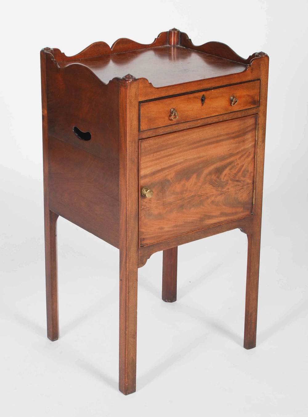 A 19th century mahogany bedside locker in George III style, the rectangular top with shaped three