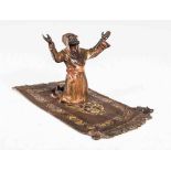 An early 20th century cold painted bronze of a figure praying on a Persian rug, in the manner of