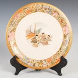 A Japanese Satsuma pottery plate, Mieji Period, decorated with figures decorating vases, within a